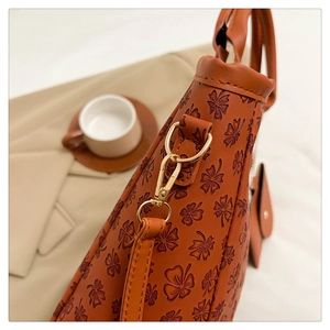 Detail of caramel leather tote with clover embossing and gold metal buckles
