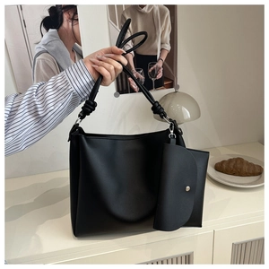 Detail of minimalist black leather bucket bag with creative knotted rope strap and mini pouch