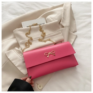 Close-up of bright pink leather envelope bag with gold bow clasp on beige blazer