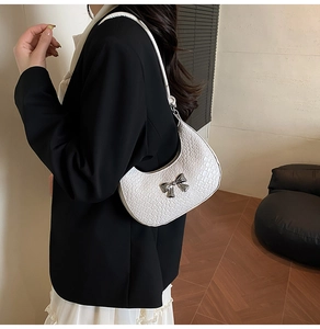 Close-up of white croc-embossed crescent bag with silver bow detail on model shoulder