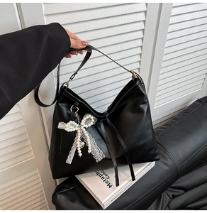Close-up of black leather hobo bag with white lace bow and pearl bead accessory