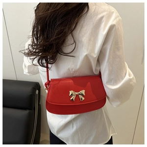 Détail d'un sac à bandoulière rouge avec fermoir doré en nœud et cuir synthétique lisse