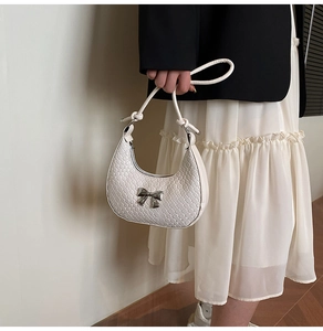 Detail of white woven crescent bag with silver metal bow and knotted shoulder strap
