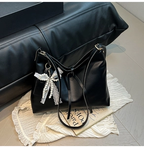 Close-up of black leather tote bag with pearl lace bow charm and knotted strap detail