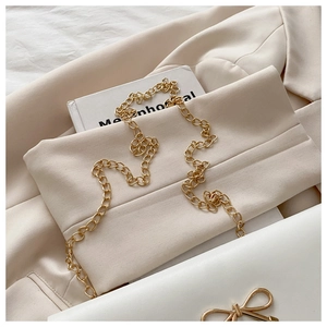 Close-up of white shoulder bag featuring gold bow-knot clasp and sleek metal chain