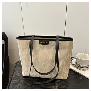 Close-up of cream tote bag with unique pleated texture, black leather trim and gold FASHION tag