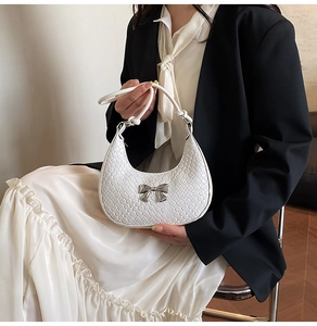 Close-up of woven white half-moon bag with silver bow detail and knot handle design