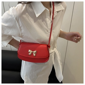 Détail du sac bandoulière rouge avec fermoir nœud doré sur chemise blanche