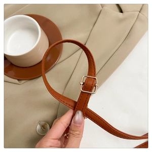 Detail of brown leather bag strap with a square gold metal buckle and neat stitching