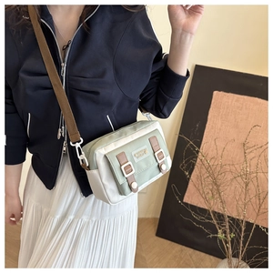 Detail van lichtgroene canvas crossbodytas met magnetische flappen en leren riemen op model