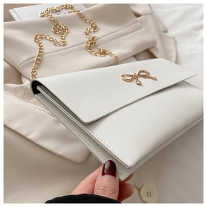 Close-up of a cream envelope crossbody bag featuring a golden metal bow and chain strap