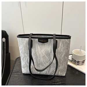 Close-up of silver pleated tote bag with black leather trim and gold FASHION text detail
