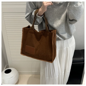 Close-up of brown corduroy tote bag featuring a leather logo patch and vertical texture