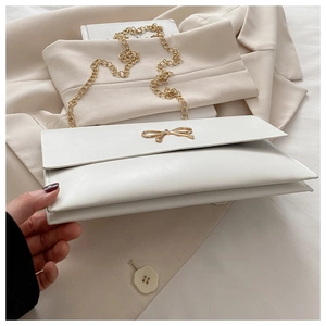 Detail of white leather crossbody bag featuring golden bow clasp and delicate chain strap