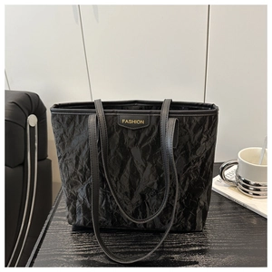 Detail of black tote bag featuring unique pleated texture and fashion logo on a desk