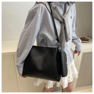 Minimalist black matte leather bucket bag with matching small pouch on female shoulder