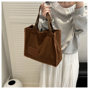 Detail of a large brown corduroy tote bag showing its rich ribbed texture and leather tag