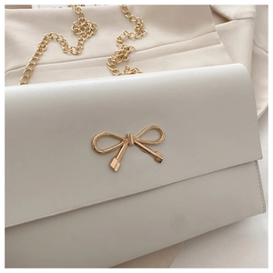 Detail of off-white PU leather bag with golden bow clasp and metallic chain strap