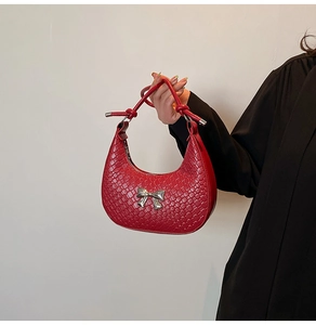 Detailed close-up of red crescent bag with woven texture and silver metal bow detail