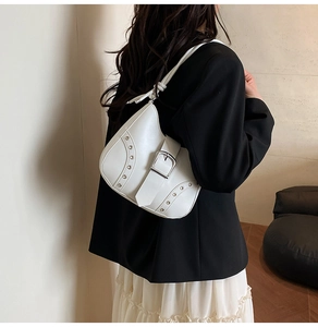 Detail of white leather baguette bag with silver studs and buckle on woman's shoulder