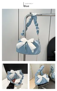 Detail of blue pleated shoulder bag featuring a large white satin bow and golden chain strap