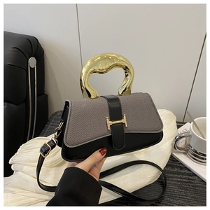 Close-up of stylish two-tone square handbag with artistic gold handle and metal buckle