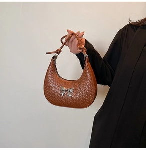 Detail of brown woven hobo bag featuring silver bow buckle and knotted handle