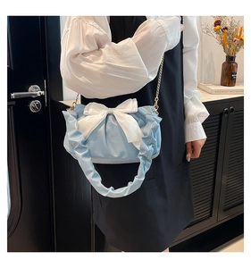 Detail showing a light blue ruched handbag with a large white bow and a gold chain strap