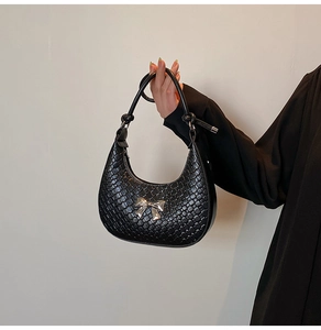 Detail of black woven hobo bag featuring a silver metal bow and knotted shoulder strap