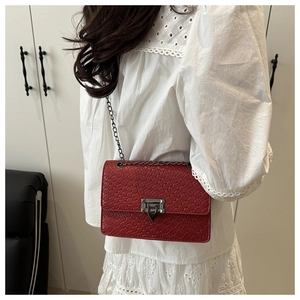 Close-up of red woven texture handbag with metal chain strap and luxury clasp detail