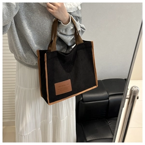Detailed close-up of a black corduroy tote bag with brown trim and fashion logo