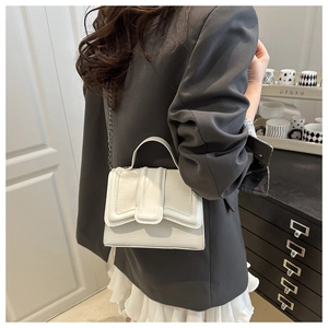 Detail of white crocodile texture handbag with metal chain strap worn by a model