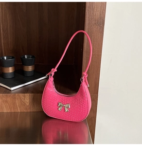 Detailed macro view of the hot pink crescent bag with crocodile texture and metal bow