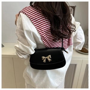 Détail d'un sac bandoulière noir avec boucle de nœud dorée sur cuir mat et lisse