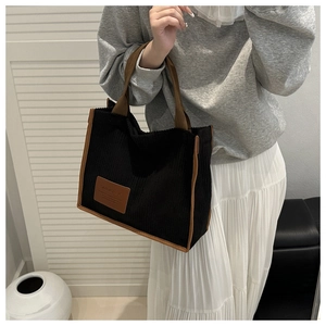 Detail of black corduroy tote bag with brown trim and vintage leather logo patch