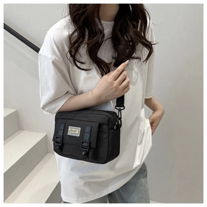Detail van de zwarte nylon crossbodytas met stijlvolle gespbanden en geborduurde logopatch
