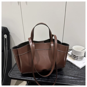 Close-up of a brown leather tote bag with white stitching detail on a modern desk