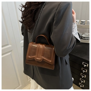 Brown crocodile embossed handbag with dark metal chain strap worn on a grey blazer