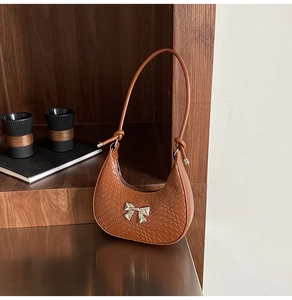 Detail of brown crocodile pattern crescent bag with silver bow accent on wooden background