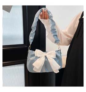 Detail of light blue pleated handbag featuring a large white satin bow and gold metal buckles