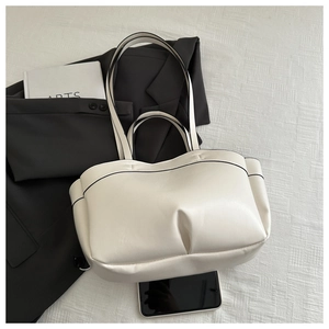 Close-up of cream tote bag with black contrast piping and stylish pleated leather texture