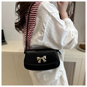 Détail d'un sac bandoulière noir minimaliste avec un fermoir nœud papillon doré chic