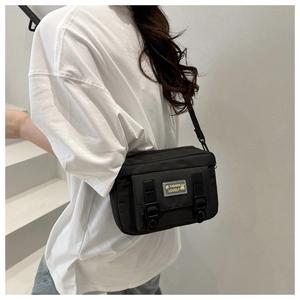 Close-up of a black nylon crossbody bag featuring a front flap and buckle hardware detail