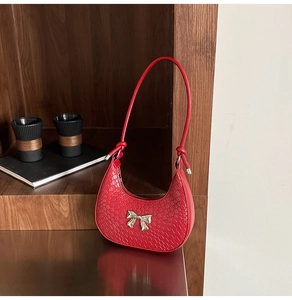 Detail of red crescent shoulder bag featuring embossed texture and a metal bow buckle
