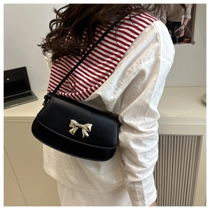 Détail du sac bandoulière noir avec fermoir noeud doré sur un cuir de finition mate