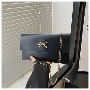 Detail of black envelope clutch featuring a gold bow accent and fine metal chain strap