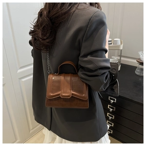Sac à main marron motif crocodile avec chaîne, porté par un mannequin dans un cadre chic