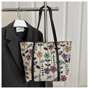 Detailed view of floral jacquard tote bag with black handles hanging on a metal hanger