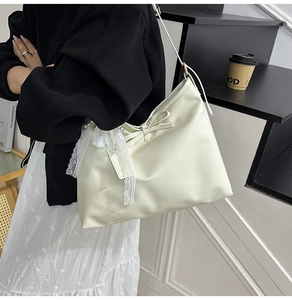 Close-up of cream tote bag with leather bow and lace pendant shown in lifestyle setting