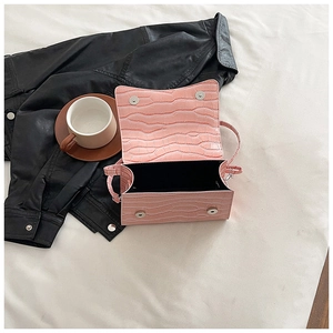 Top view of pink crocodile-textured crossbody bag with silver hardware on a leather jacket